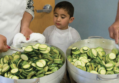 Boy watching two large pots of cooked zucchini